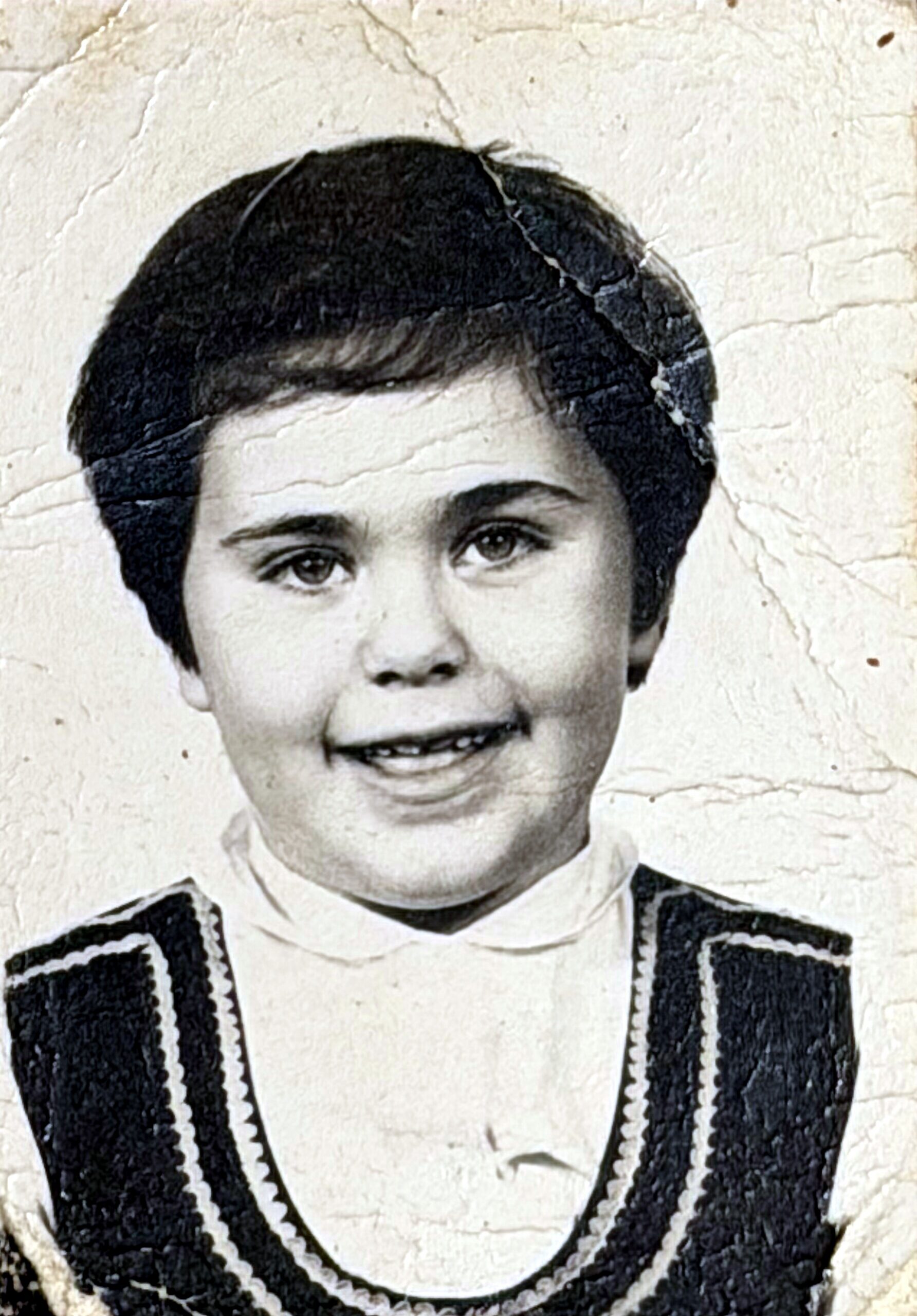 Smiling young boy with dark hair, wearing a patterned sweater in a vintage black-and-white portrait.