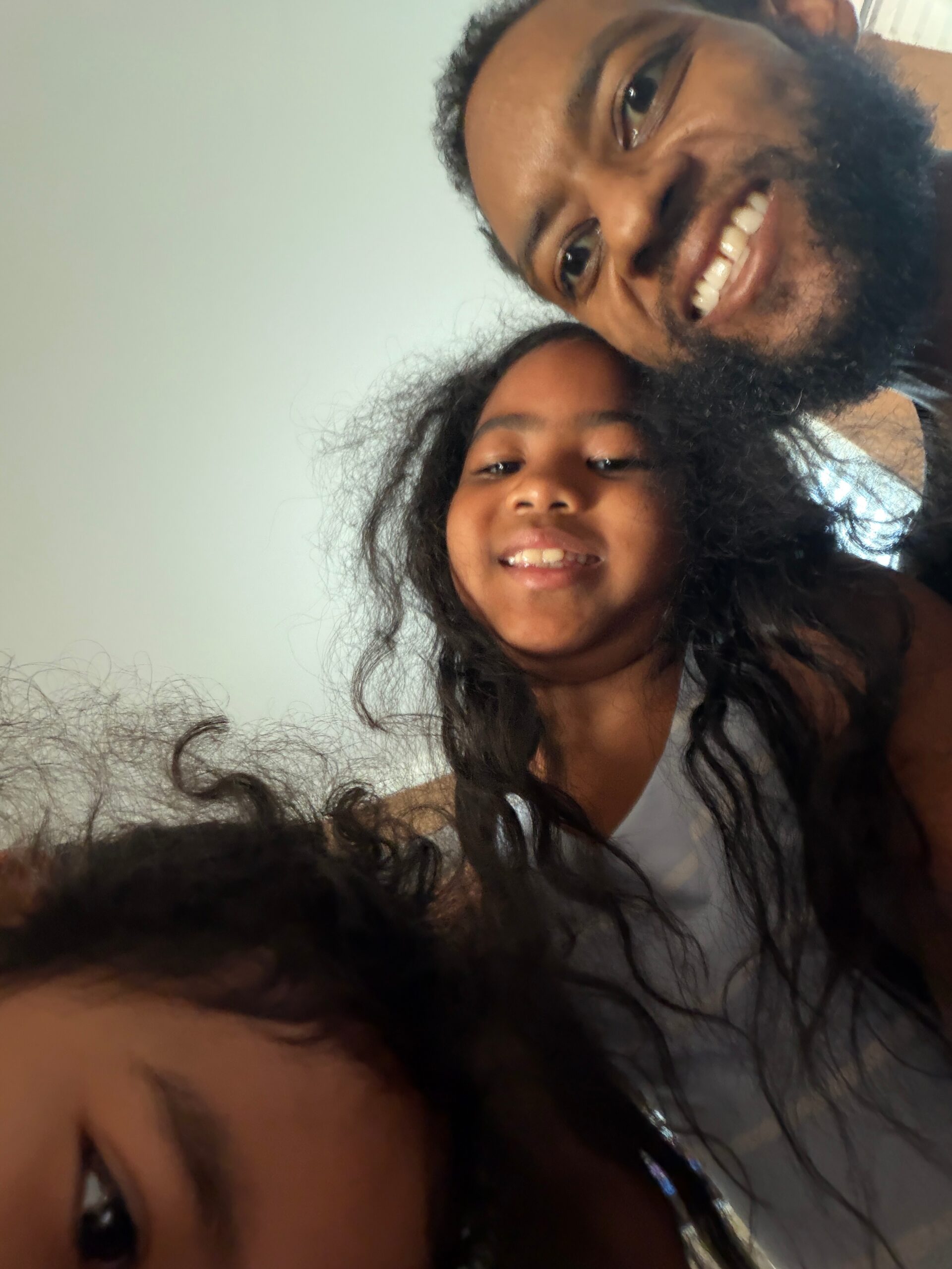 Close-up selfie of a bearded man and a smiling girl leaning in together.
