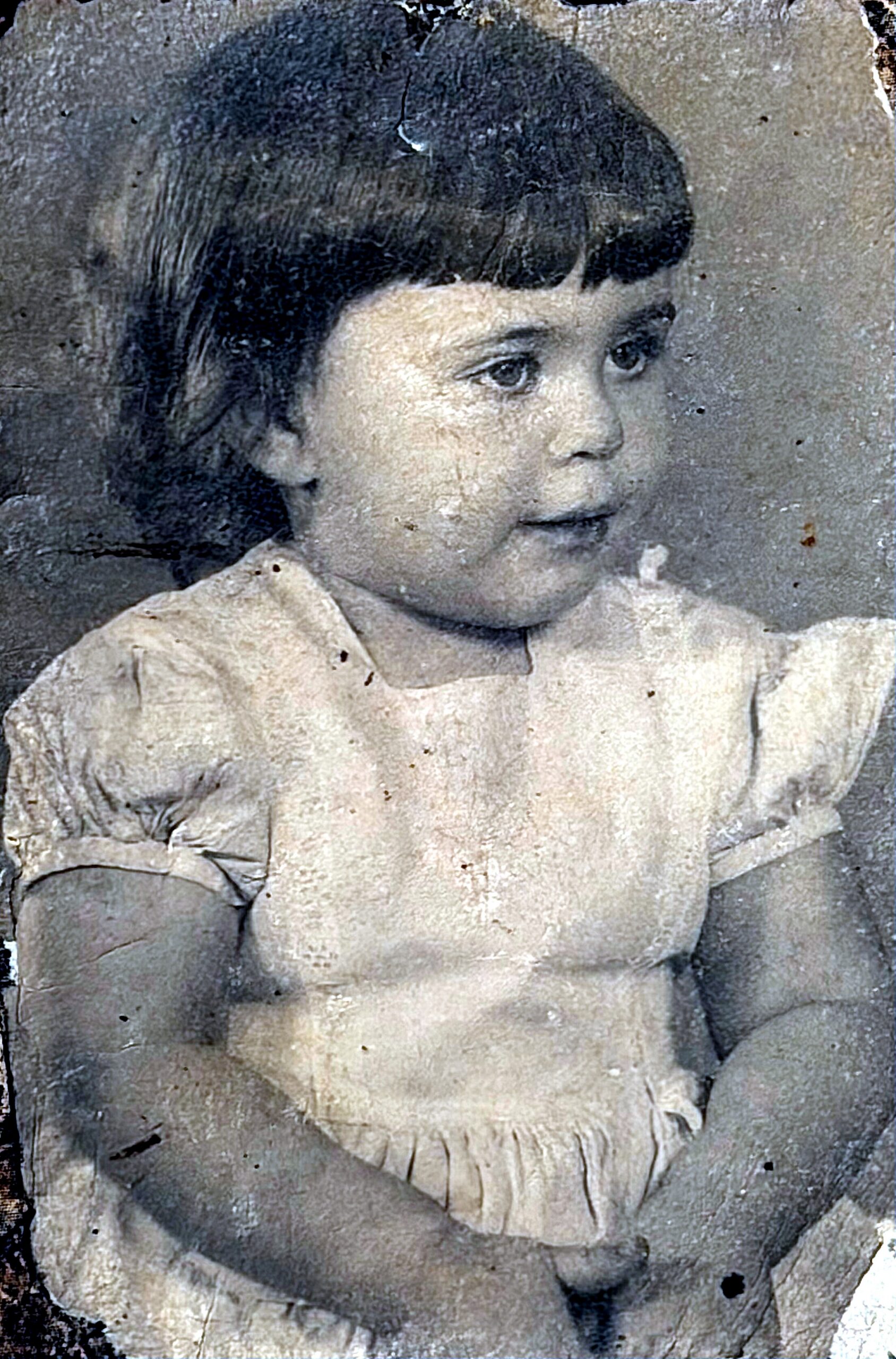 Young child with short dark hair in a light dress, looking to the right in a vintage portrait.