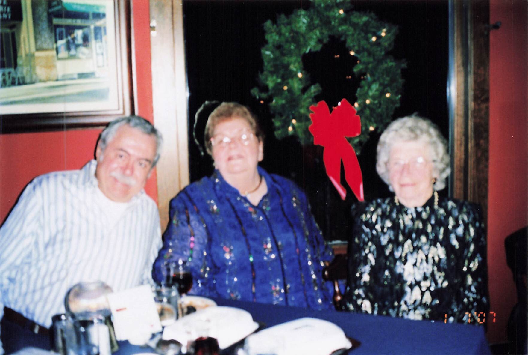 Three seniors seated at a dinner table, smiling, with a decorated tree and red wall behind them.