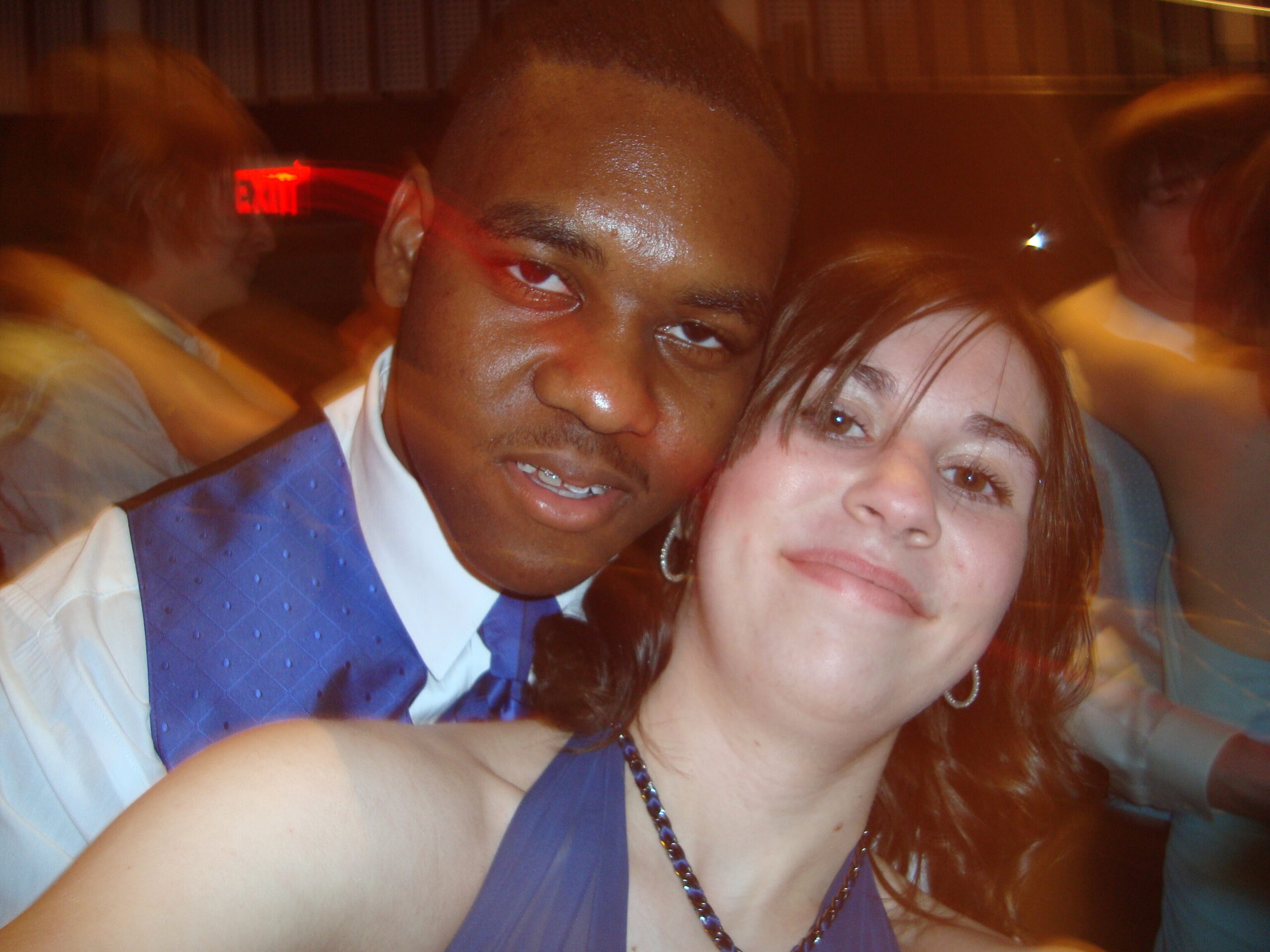 Close-up selfie of a man in a blue vest and a woman smiling at a party.