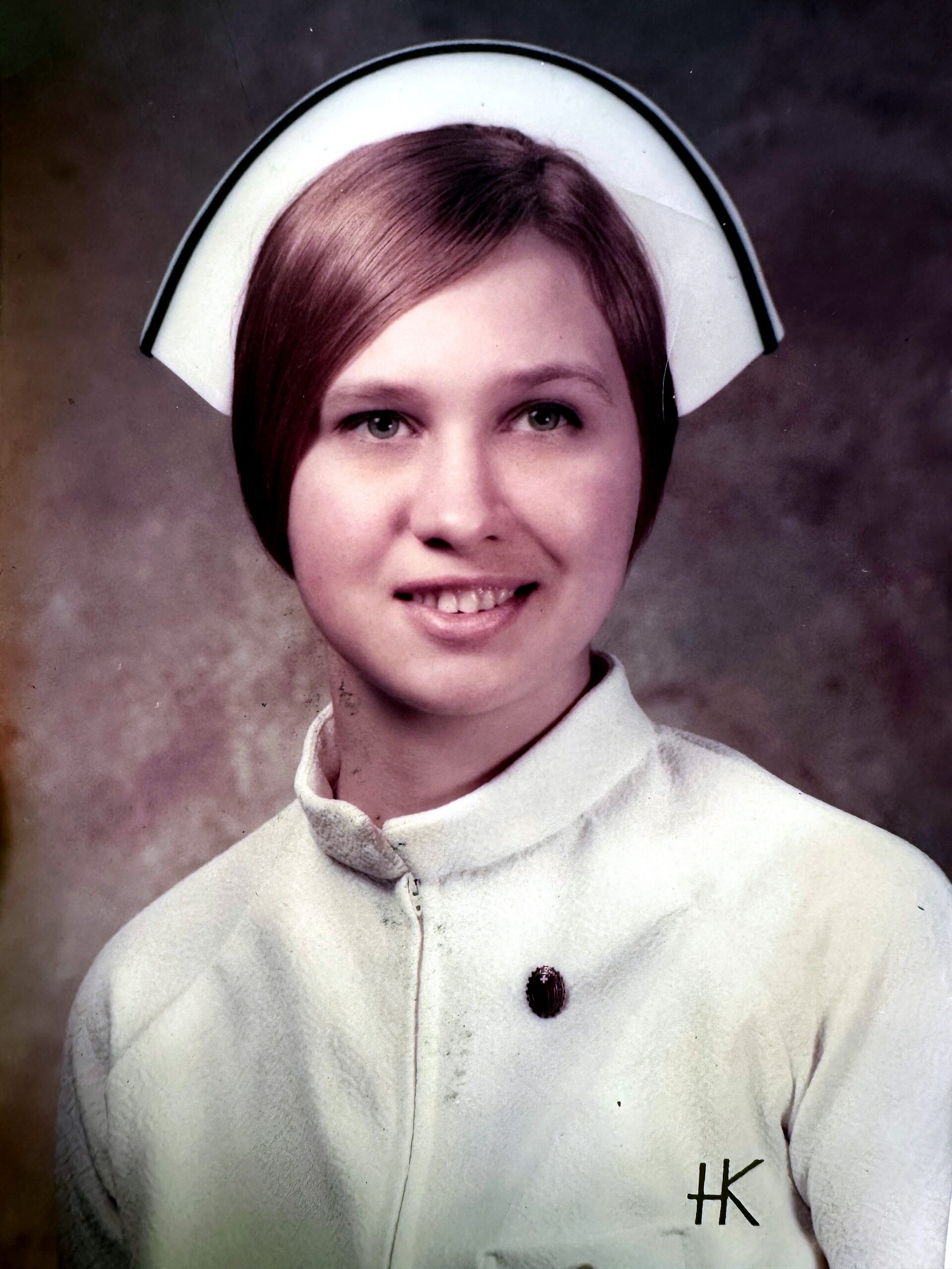 Young nurse in a white uniform and cap, smiling for a vintage studio portrait.