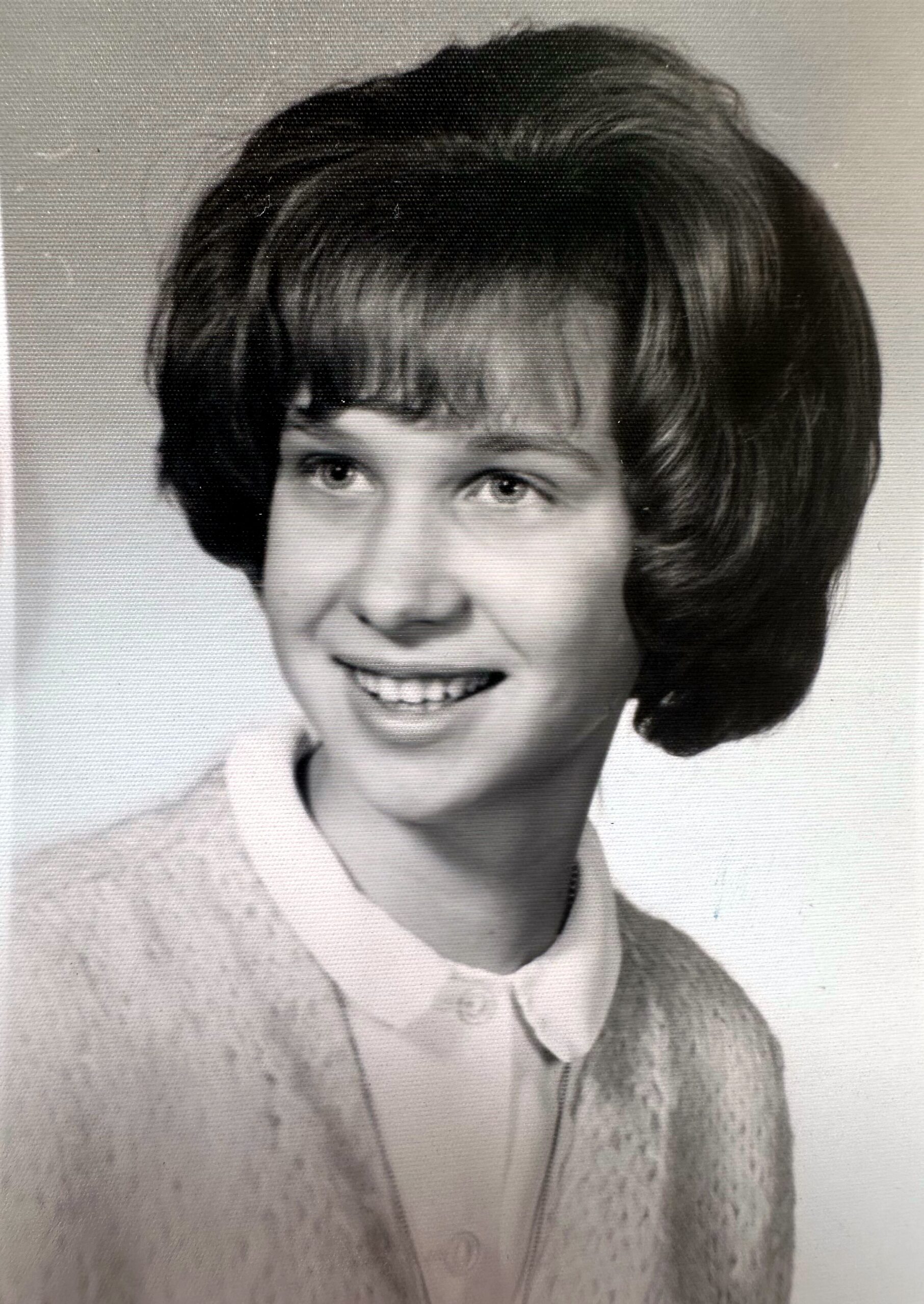 Smiling young woman with short dark hair in a black-and-white studio portrait, wearing a collared blouse and cardigan.