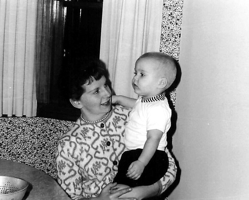 Woman holding a baby on her lap, smiling at each other in a domestic room.