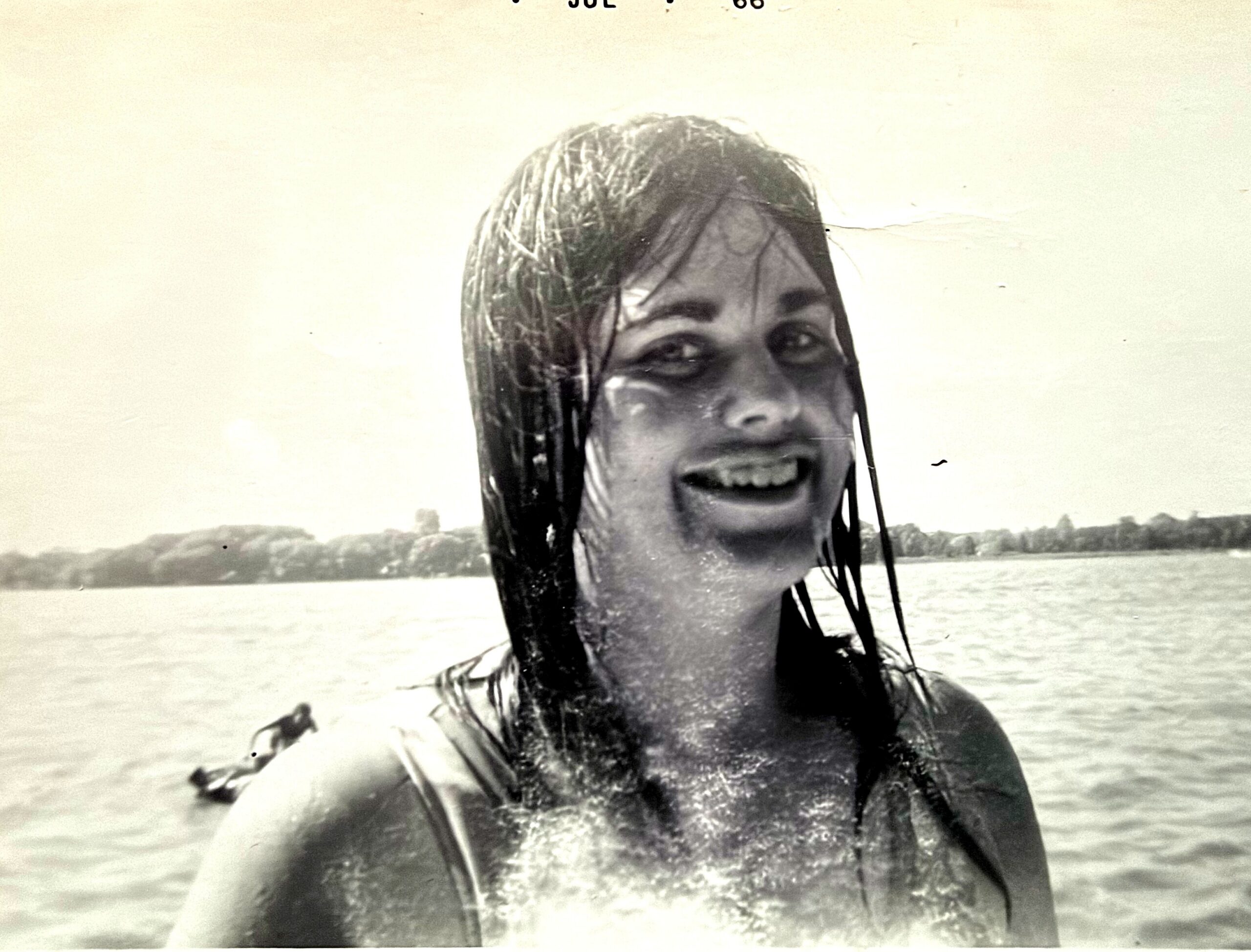 Smiling woman with wet hair at the beach, shoreline and water in the background.