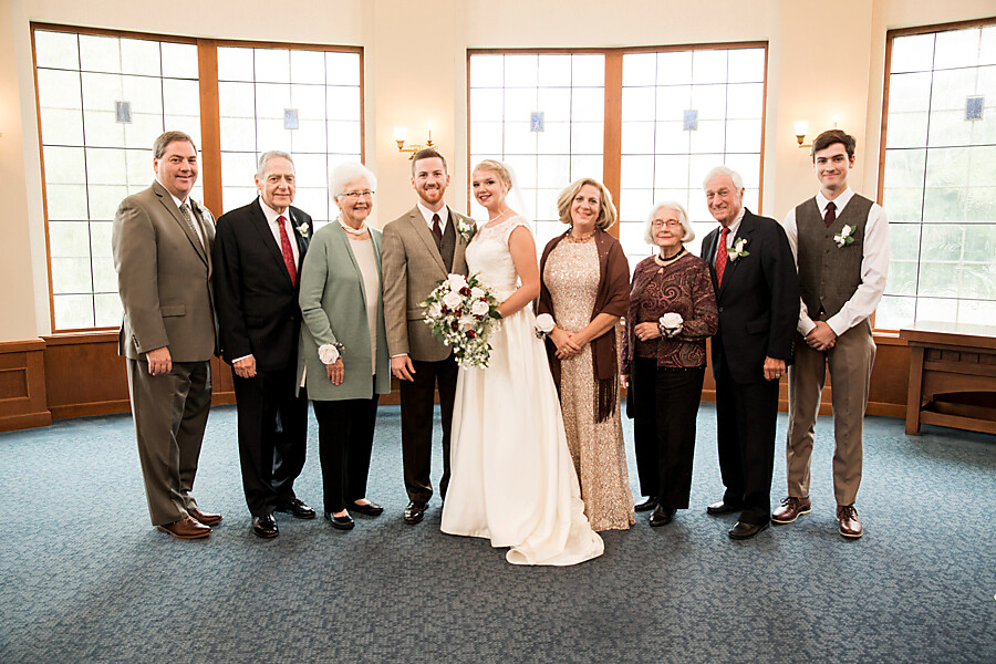 Bride and groom pose with family in a warmly lit room during a wedding photo.