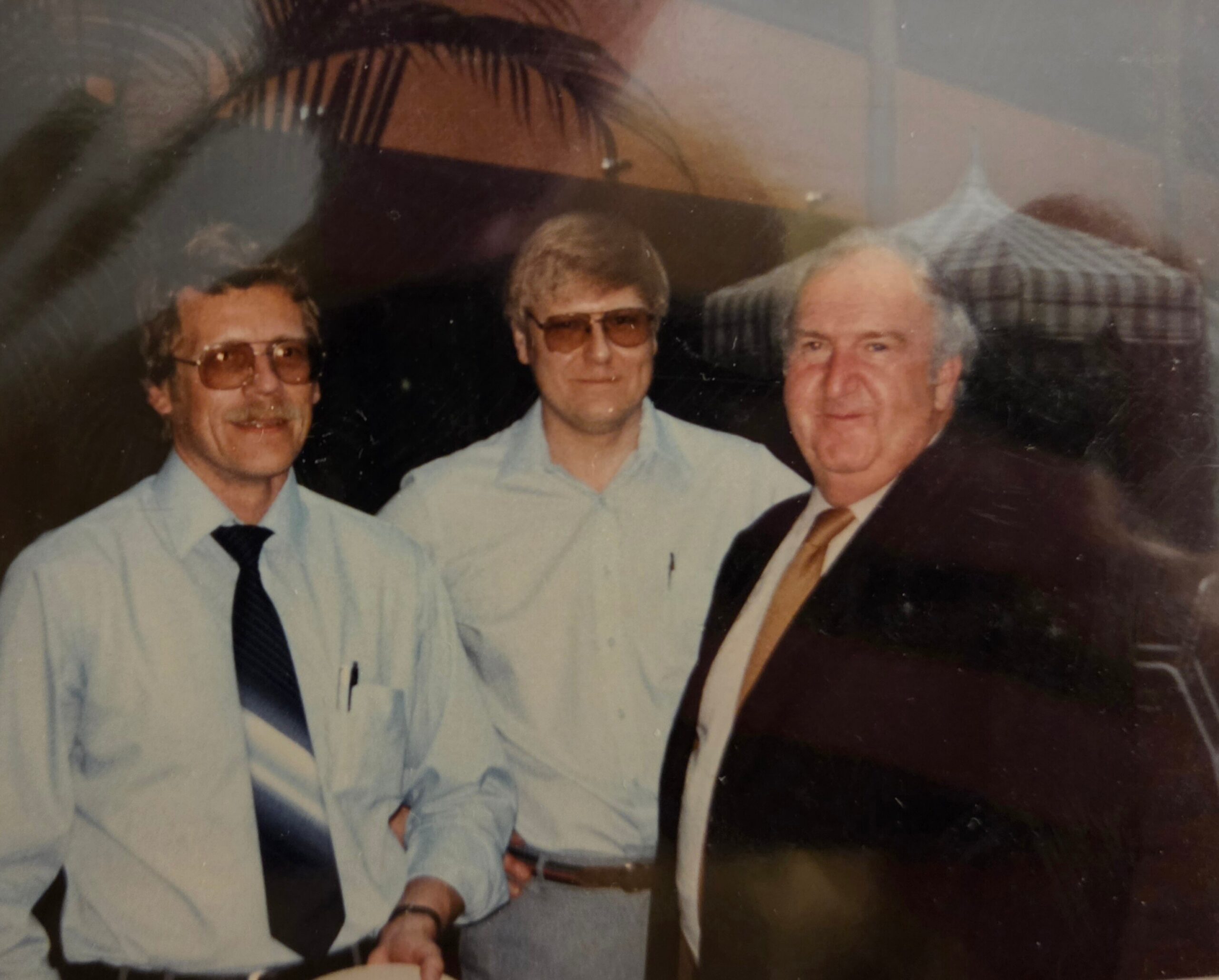 Three men in business attire posing together for a photo indoors, looking at the camera and smiling.