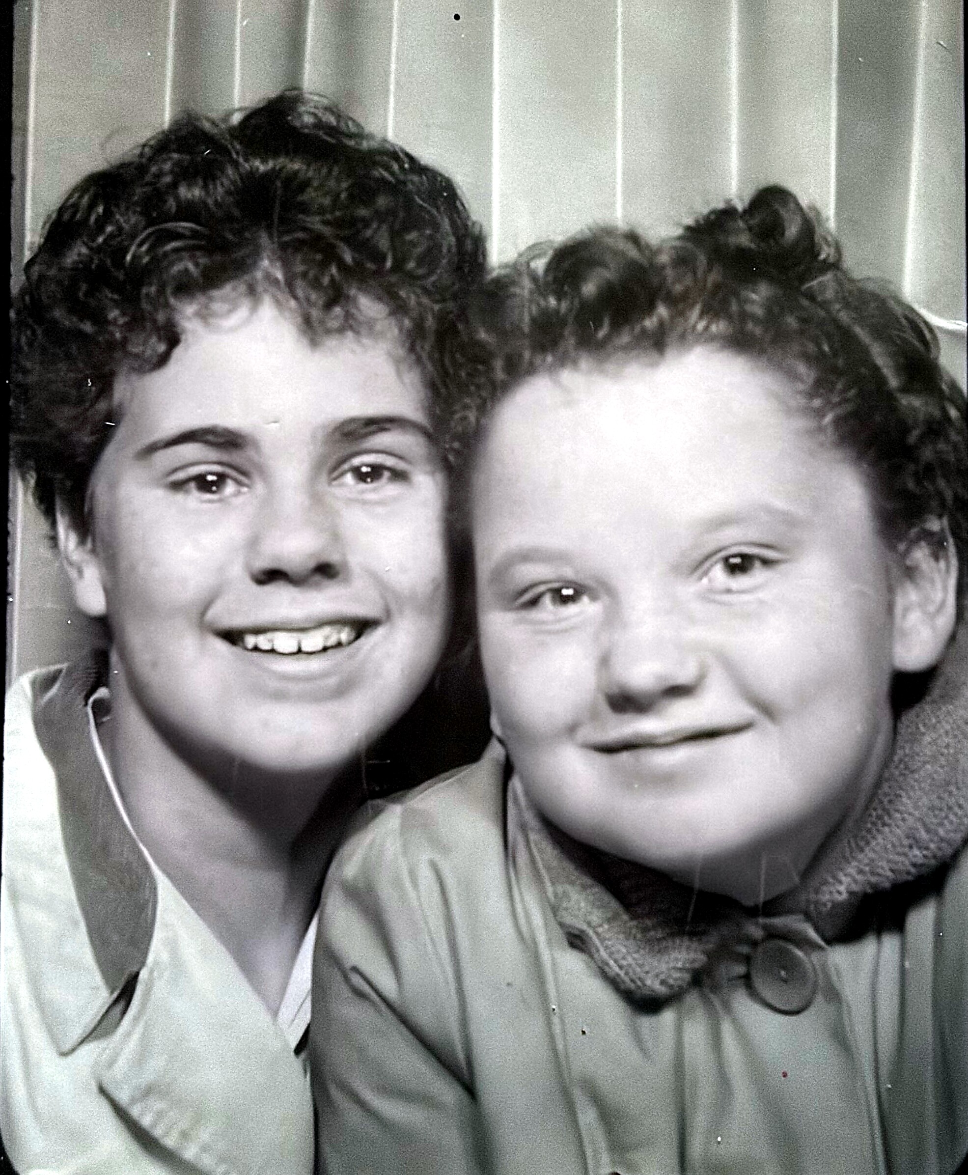 Two people close together, smiling at the camera in a black-and-white photo, wearing jackets.