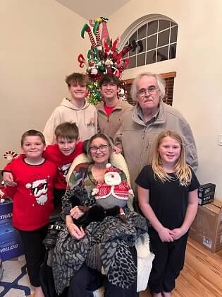 Grandmother seated in a leopard-print blanket, surrounded by six relatives posing for a Christmas photo in a living room with a decorated tree behind them.