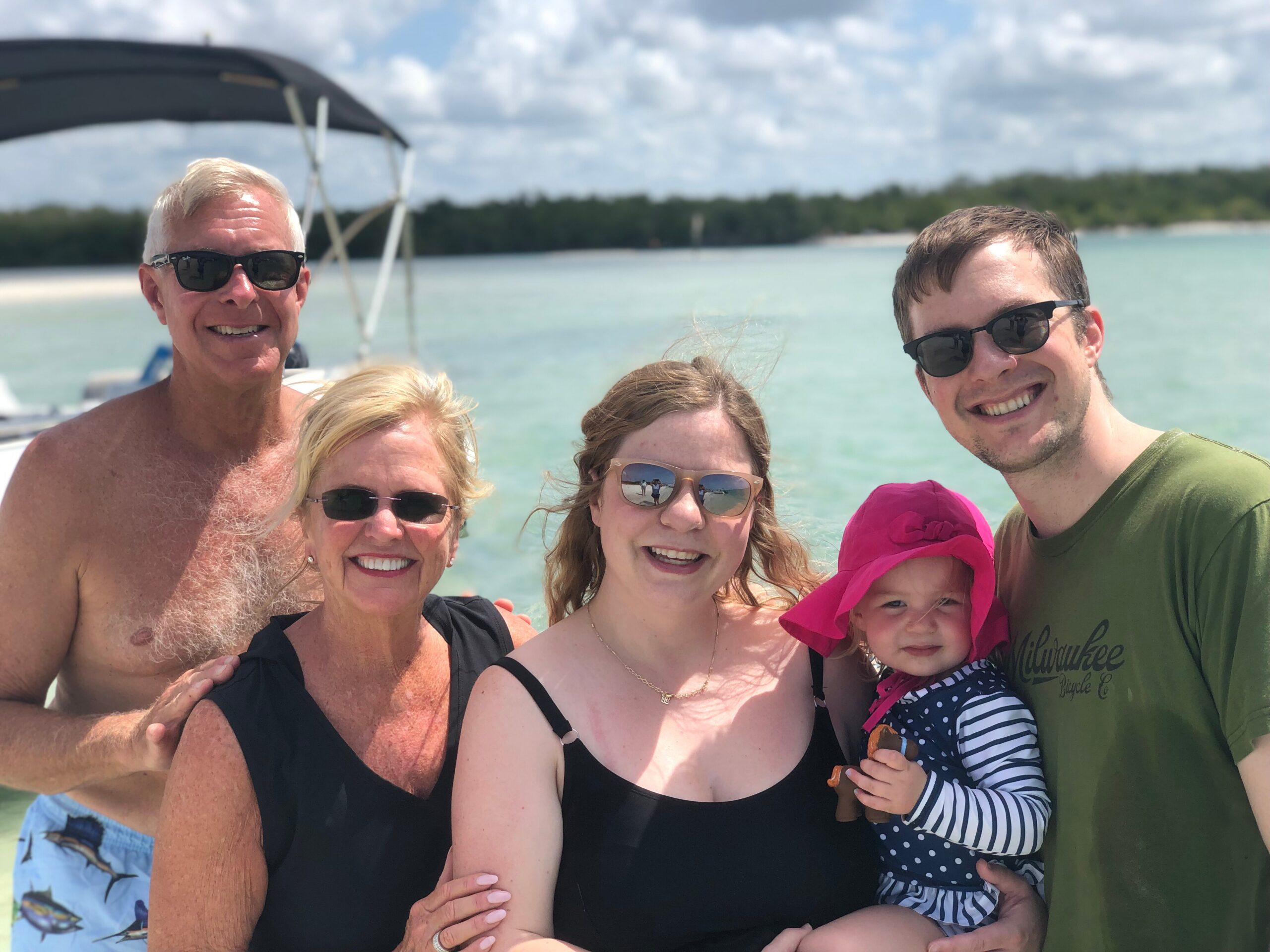 A smiling group of adults and a child posing closely on a boat with turquoise water and a sunny sky in the background.