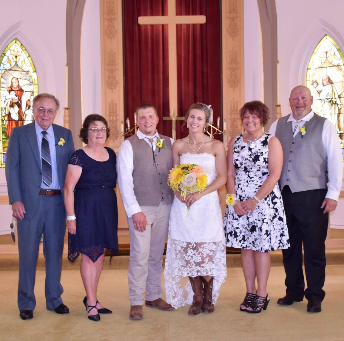 Bride and groom pose with family members inside a church, holding bouquets and smiling in front of a cross backdrop.