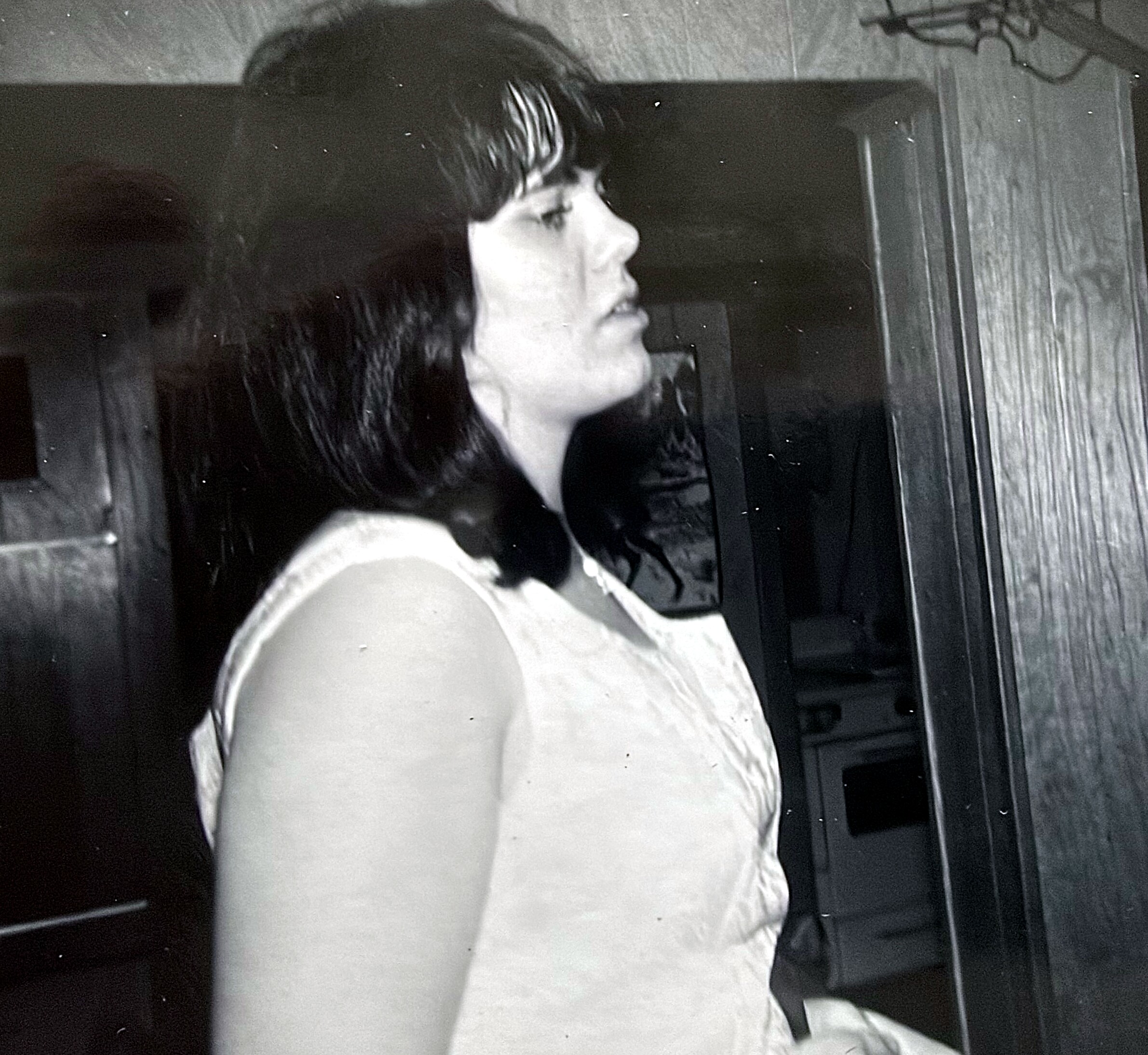 Side profile of a woman with wavy dark hair wearing a light sleeveless top, in a grayscale photo.