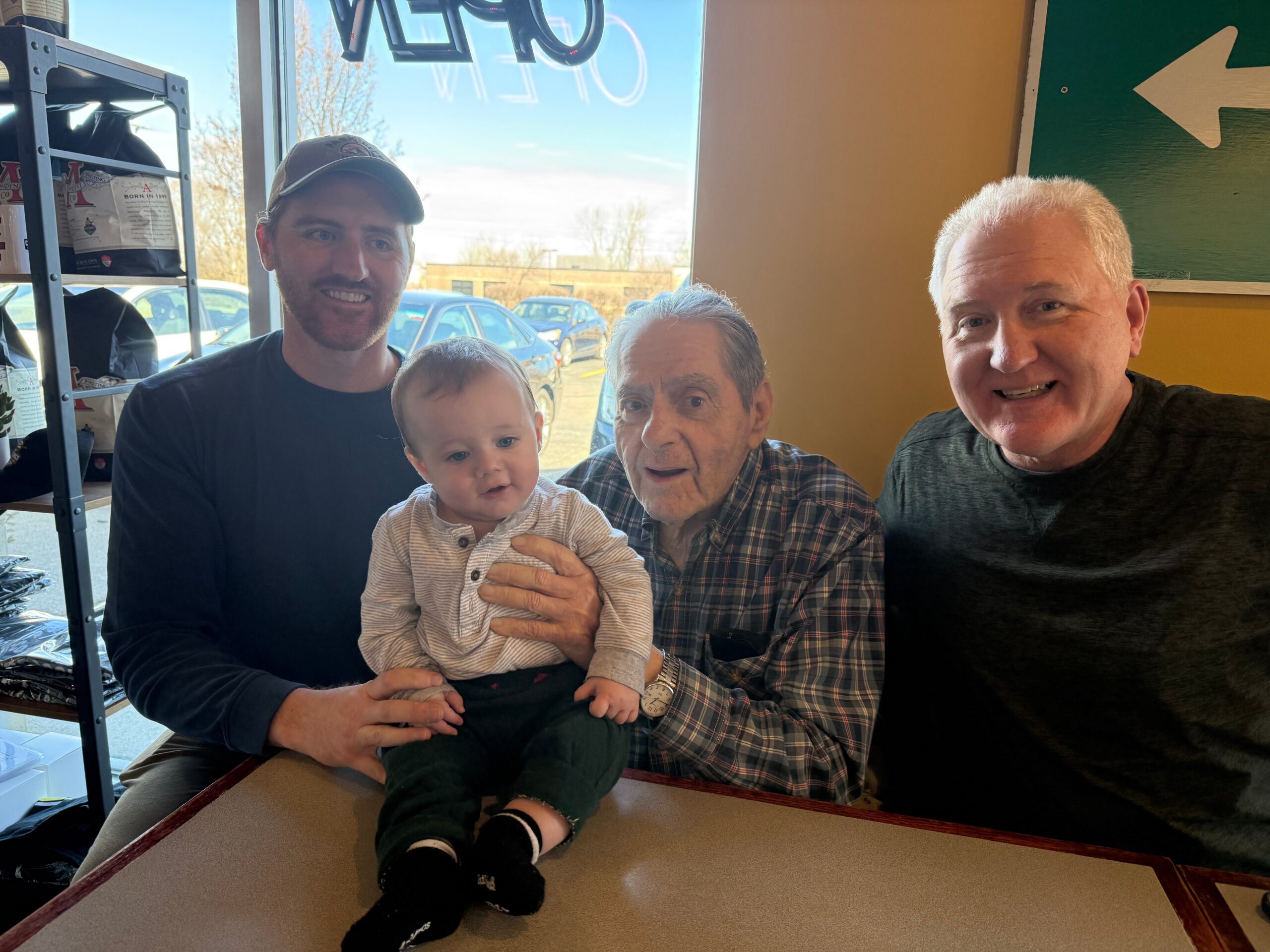 Three men and a baby posing for a selfie in a cafe.