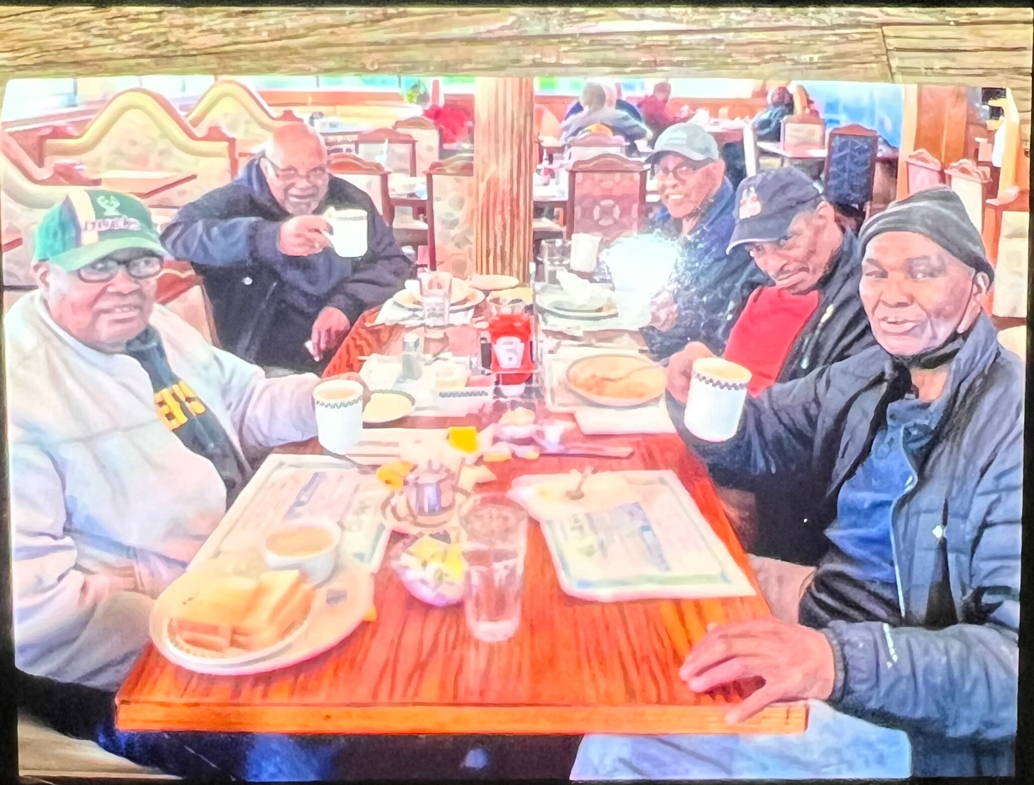Six older men sitting around a wooden table in a restaurant, smiling and enjoying drinks together.