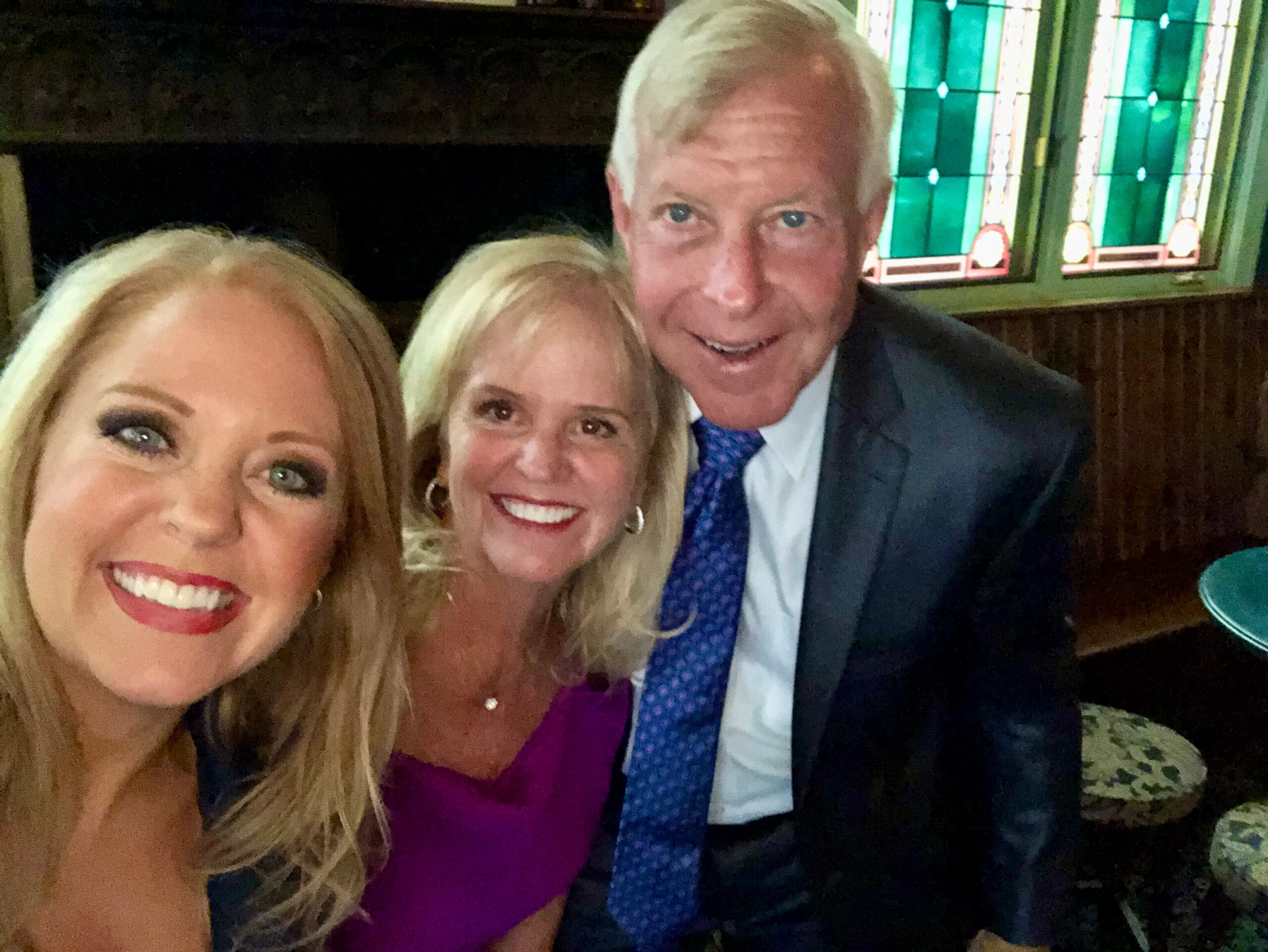 Selfie of four adults smiling for the photo indoors, with a colorful stained-glass window in the background.