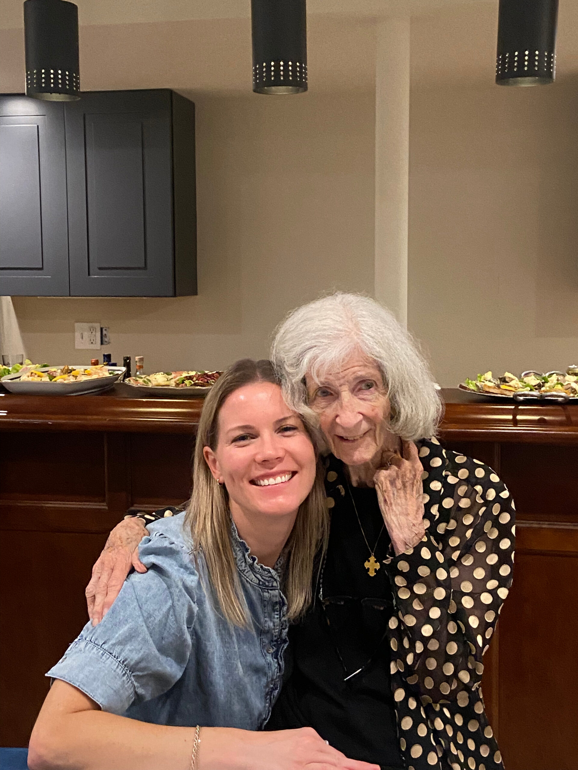 Two women smiling for a selfie at a restaurant, with buffet trays visible in the background behind them.
