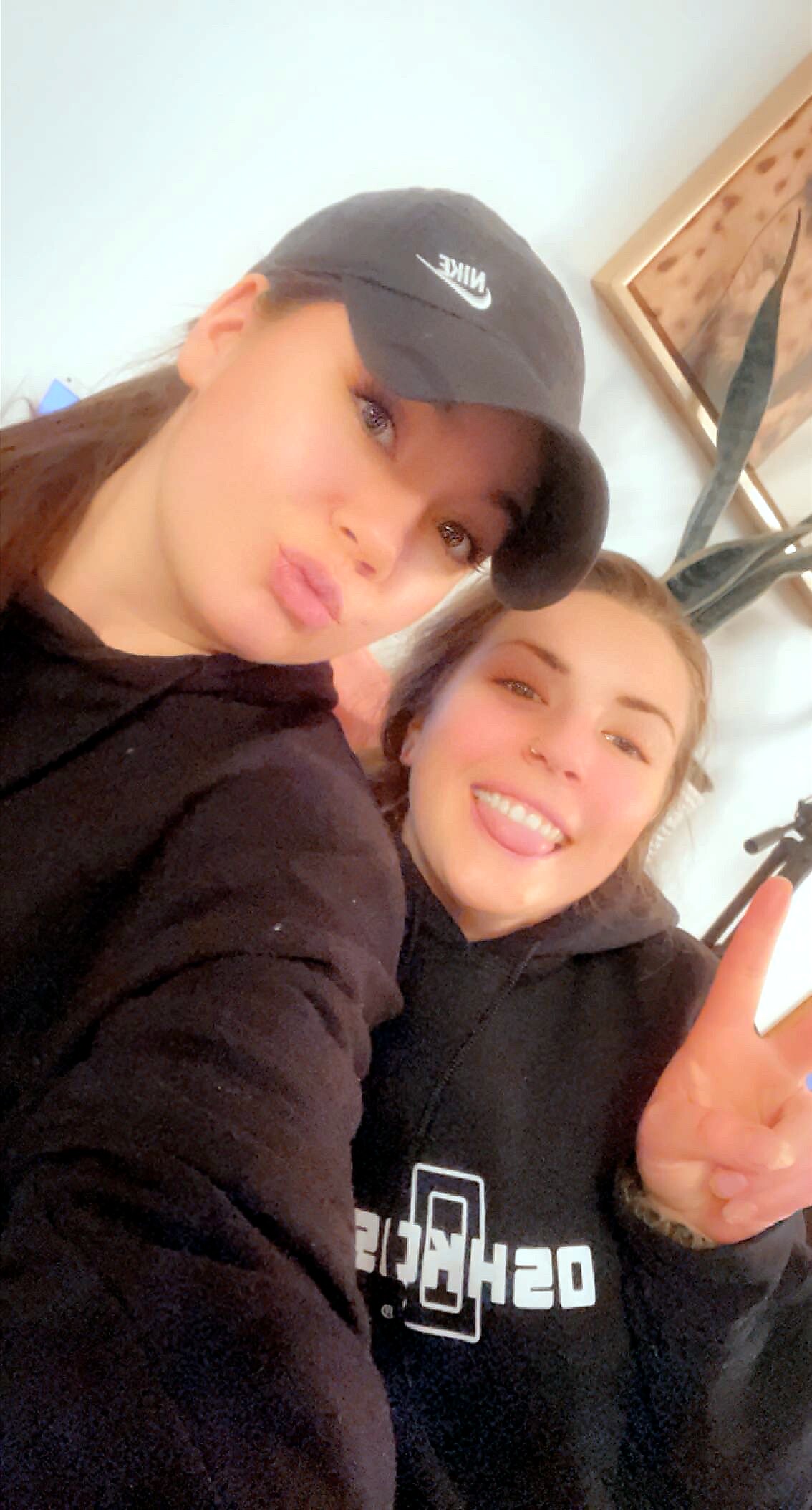 Two friends posing for a casual indoor selfie, one wearing a black Nike cap and hoodie.