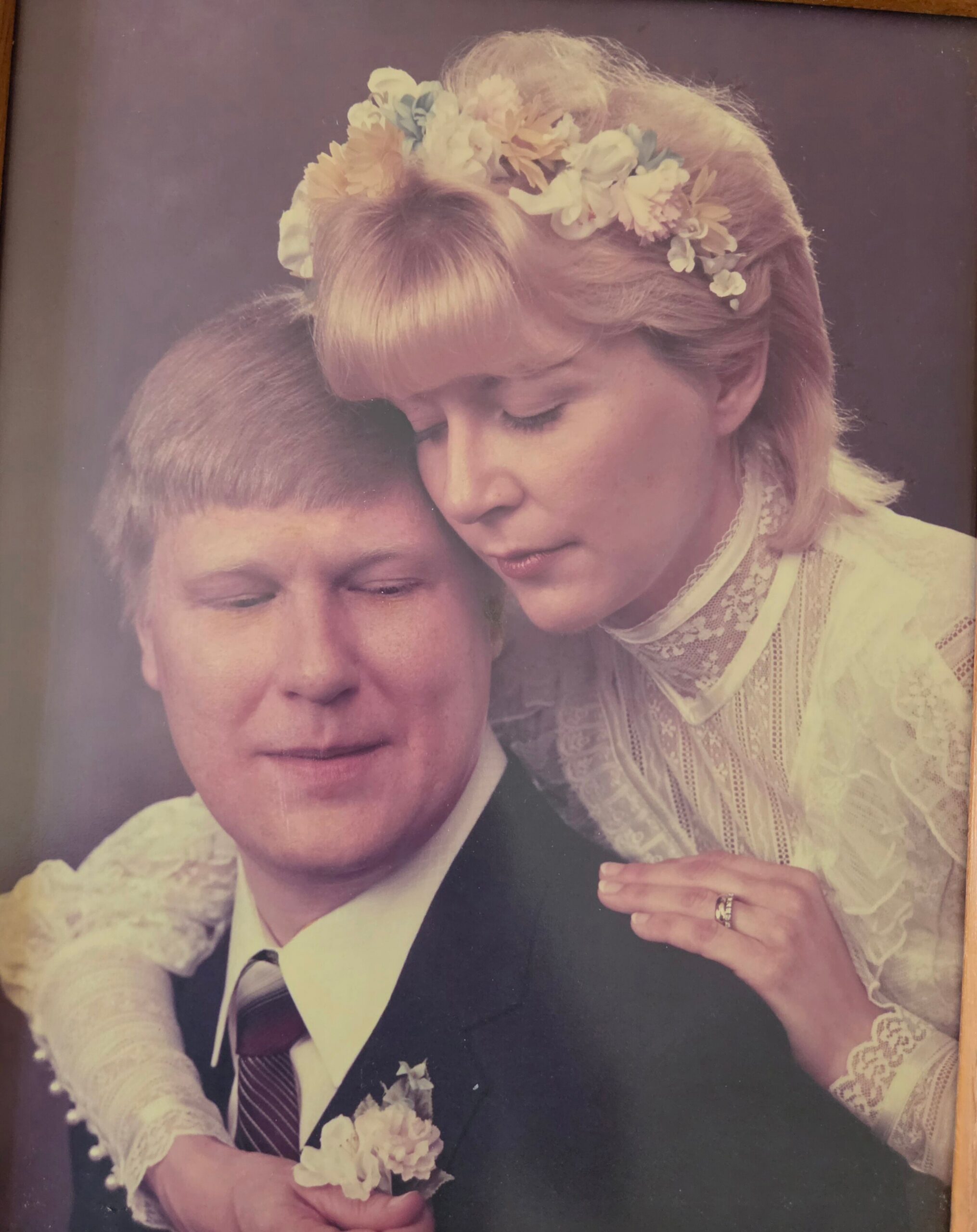 Bride rests her head on the groom's shoulder, wearing a flower crown and lace wedding dress in a tender wedding photo.
