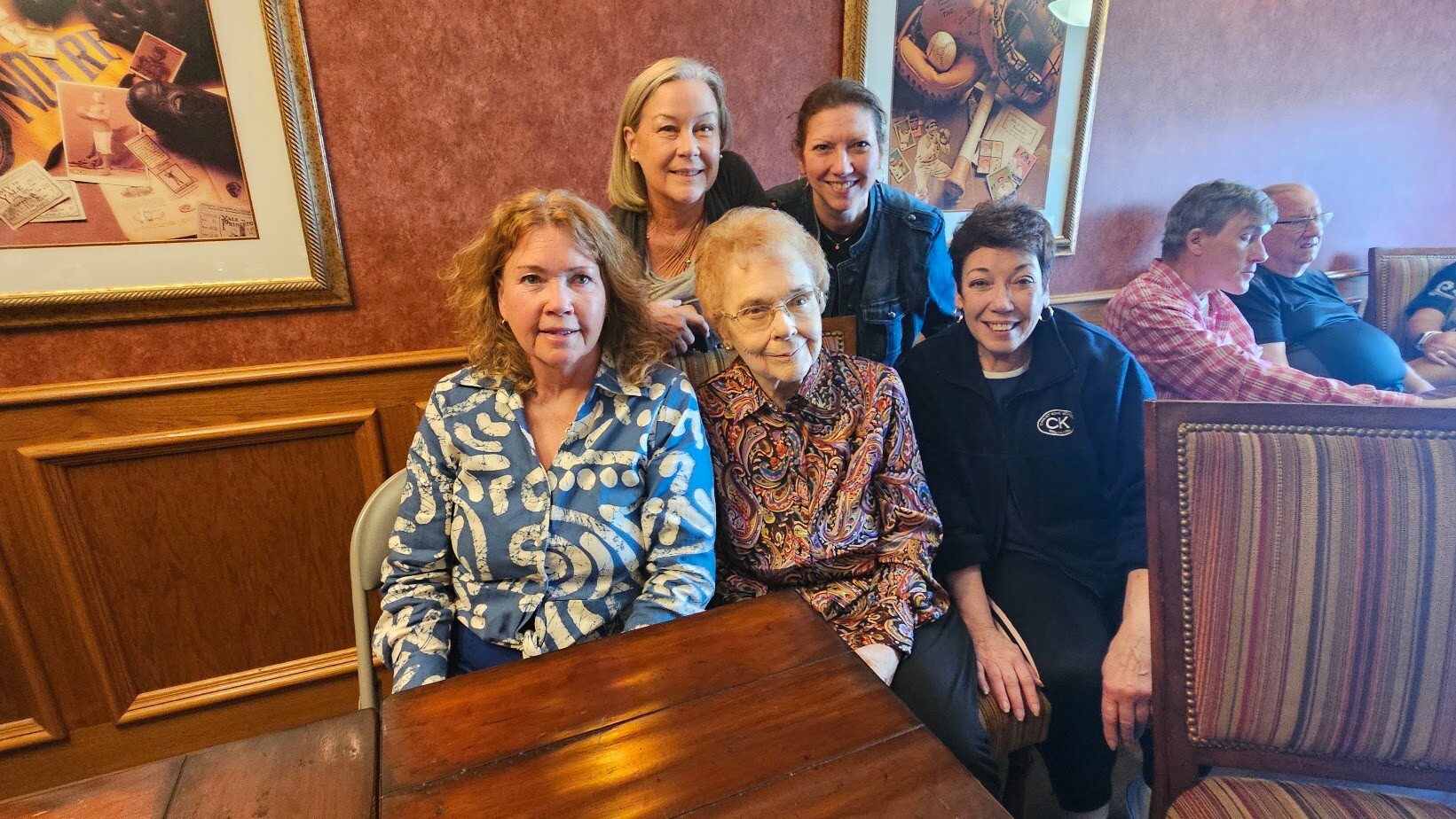 Group of adults posing for a photo in a wood-paneled restaurant, smiling at the camera.