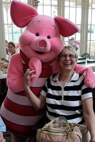 Smiling woman in a black-and-white striped shirt pose with a large pink pig mascot indoors, pig wearing red stripes and embracing her.