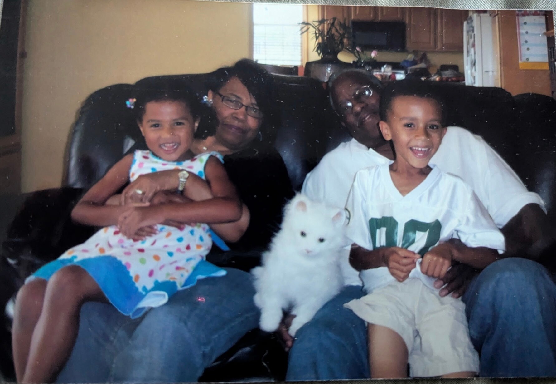 Family of four on a living-room sofa smiling at the camera, with a fluffy white dog in front.