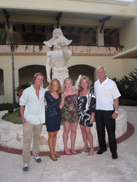 Six adults posing together in front of a large statue fountain on a resort courtyard.