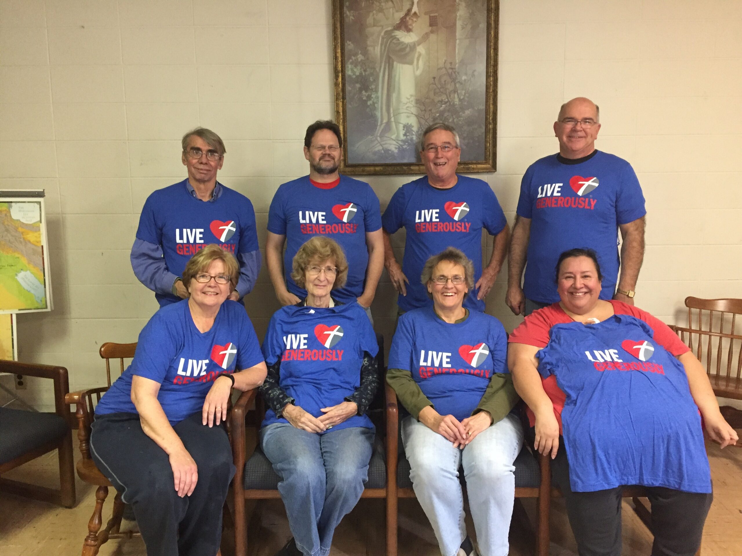 Group of adults in blue 'Live Generously' shirts posing for a group photo indoors.