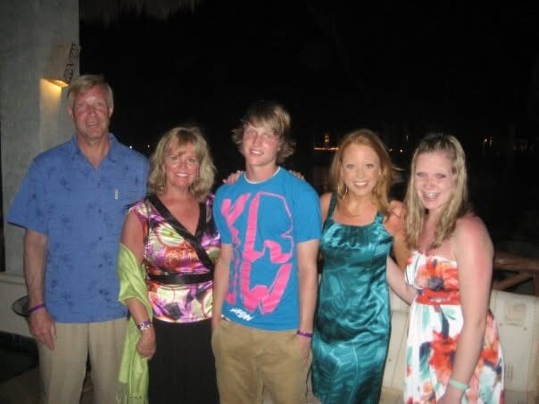 Five people posing for a photo on a dimly lit outdoor balcony at night, wearing casual summer clothes and smiling.