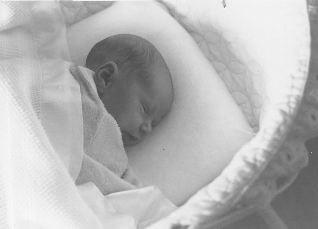 Newborn baby asleep on mother's bare chest, wrapped in soft blankets.