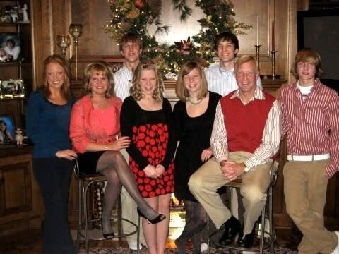 Family and friends posing for a holiday photo in a living room by a decorated Christmas tree and garland in the background.