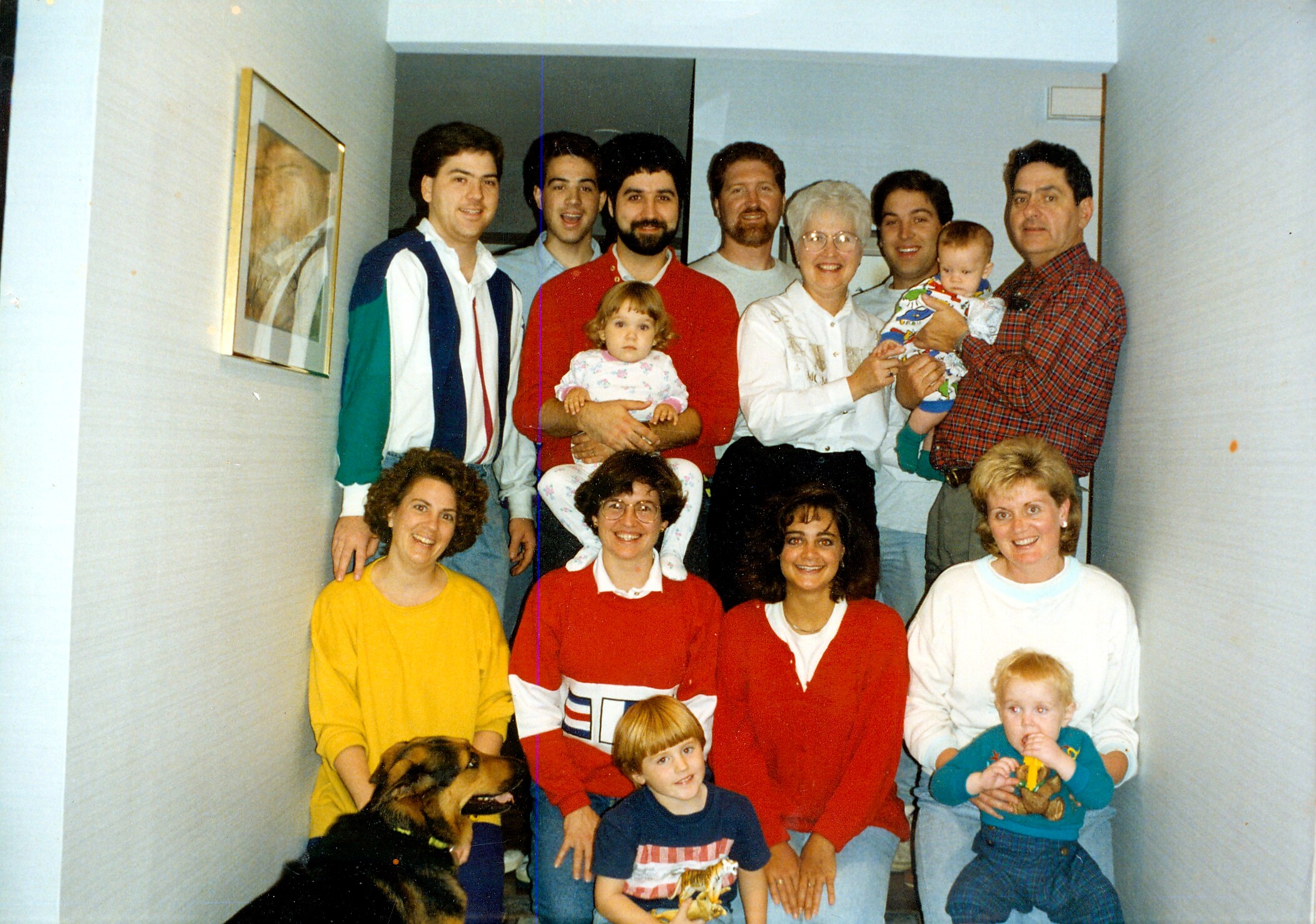 Large multi-generational family group portrait in a narrow hallway, with adults, teens, several children, and a dog in the foreground.