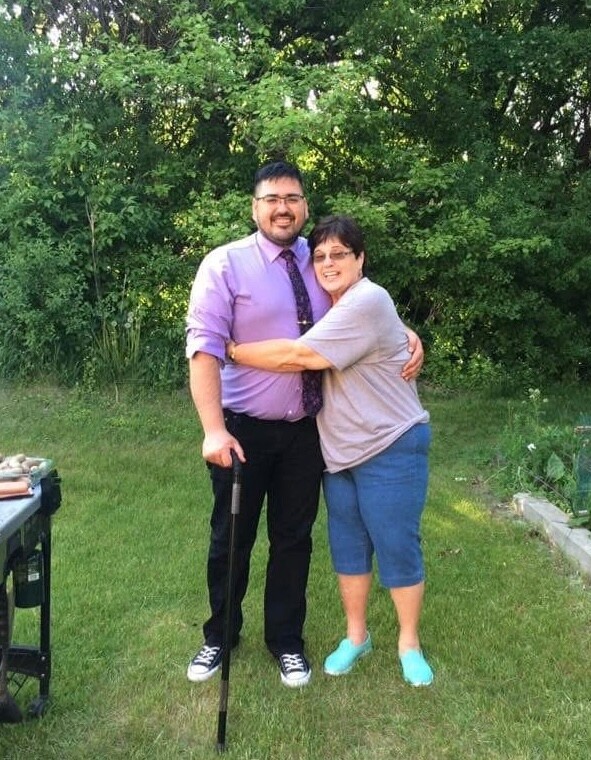 Couple smiling and hugging outdoors by a grill and green shrubs; man using a cane.