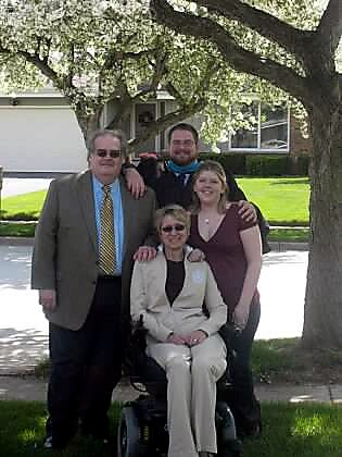 Four family members posing outdoors under a tree; an elderly woman in a wheelchair sits in front with three relatives standing around her.