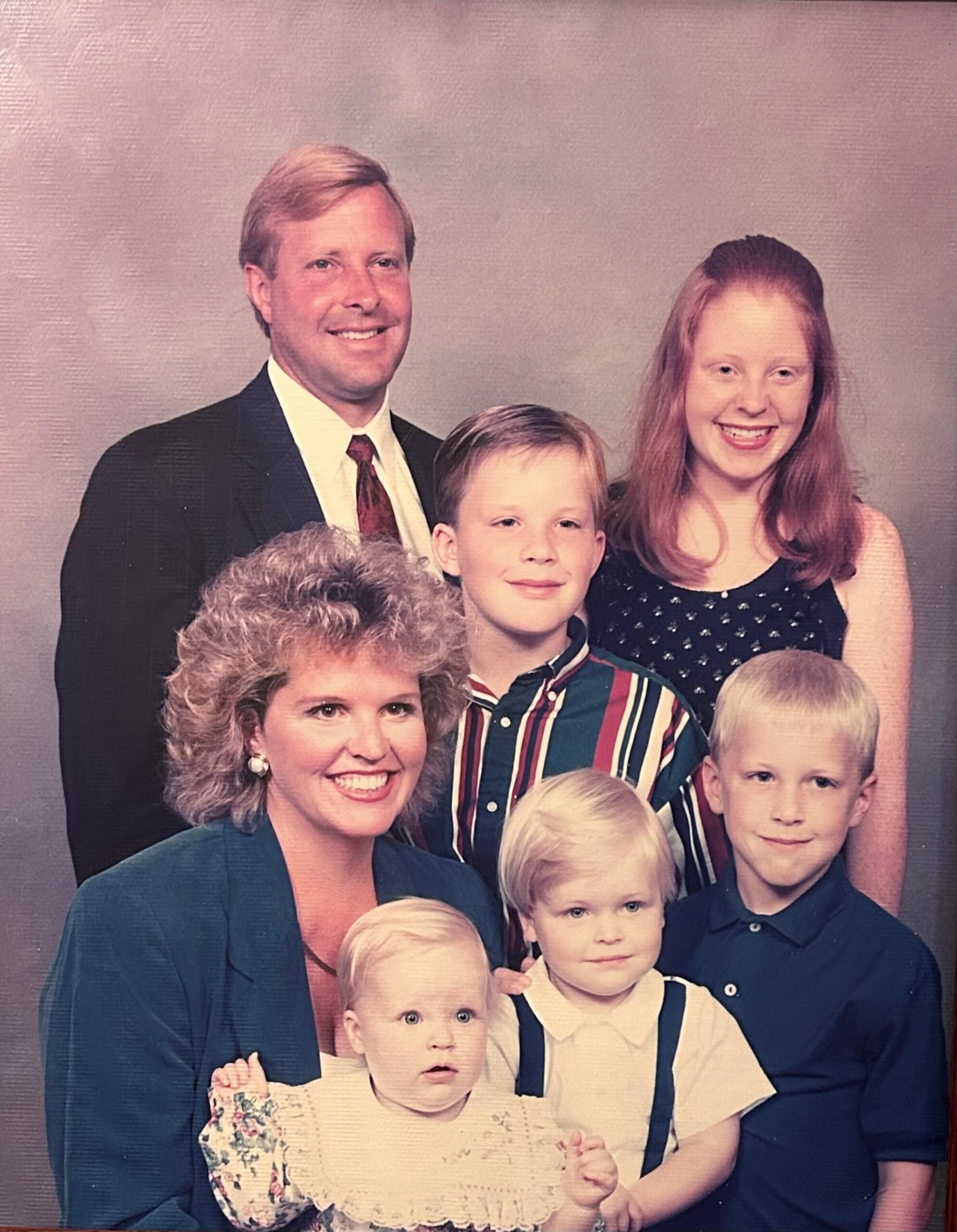 Group portrait of a multi-generational family posing together in a studio backdrop, including grandparents and several children.