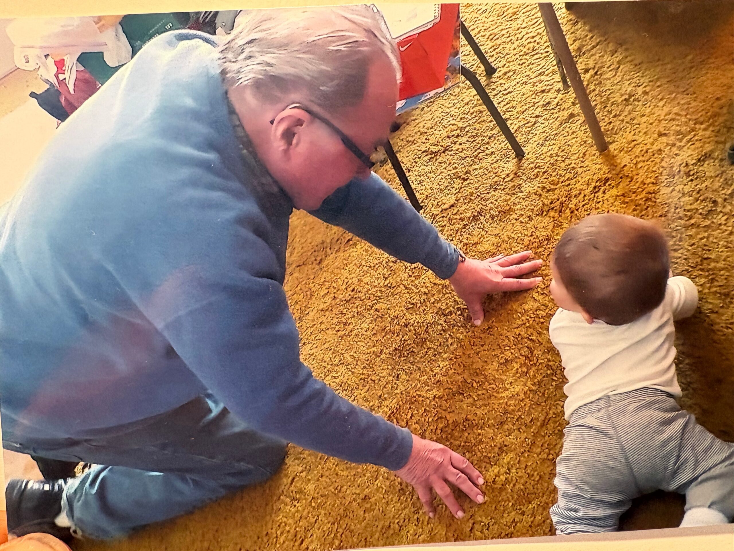 Top-down view of an adult in a blue shirt and a small child on a brown carpet, their hands reaching toward the center.