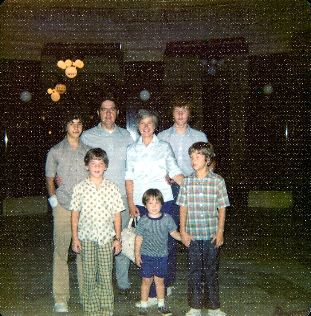 Family group posing for a photo at an indoor party, with Mickey Mouse balloons in the background.