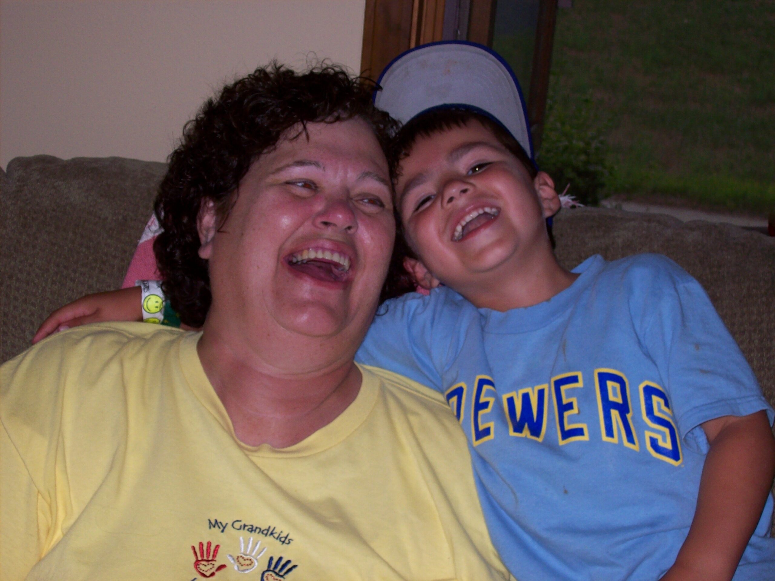 Adult woman and young boy smiling at the camera while leaning on a couch indoors.