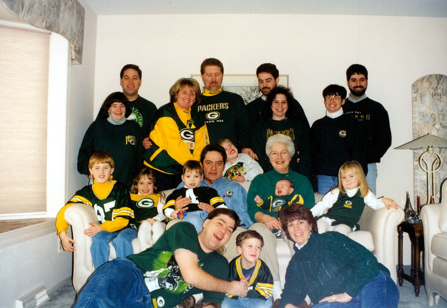 Large family gathering in Green Bay Packers gear posing in a living room.