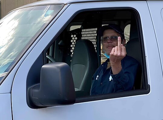 Man in a white van raises a middle finger from the driver's seat, visible through the open window, gesture appears defiant.