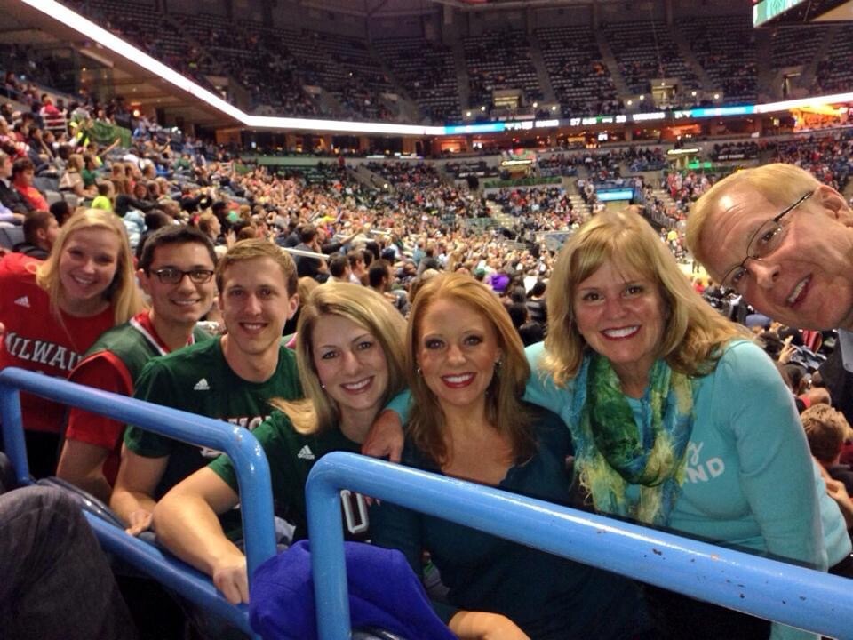 Group of six smiling people posing for a photo in a crowded sports arena with spectators in the background.