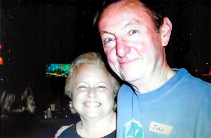 Smiling man in a blue shirt with a nametag posing with a smiling woman at a nighttime event.
