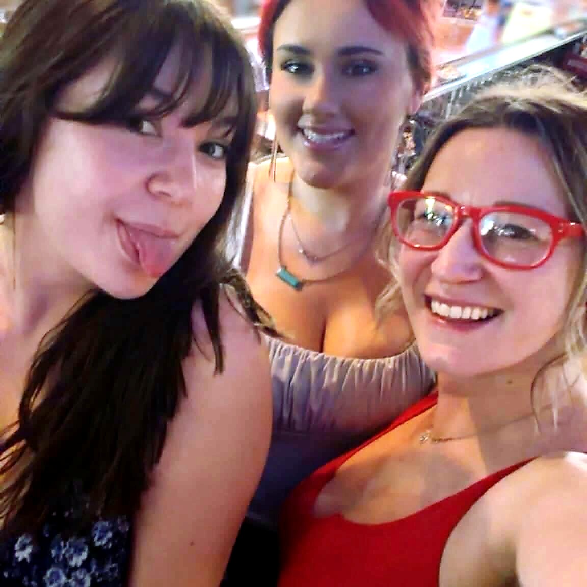 Three women taking a playful selfie, one sticking out her tongue while the others smile at the camera.