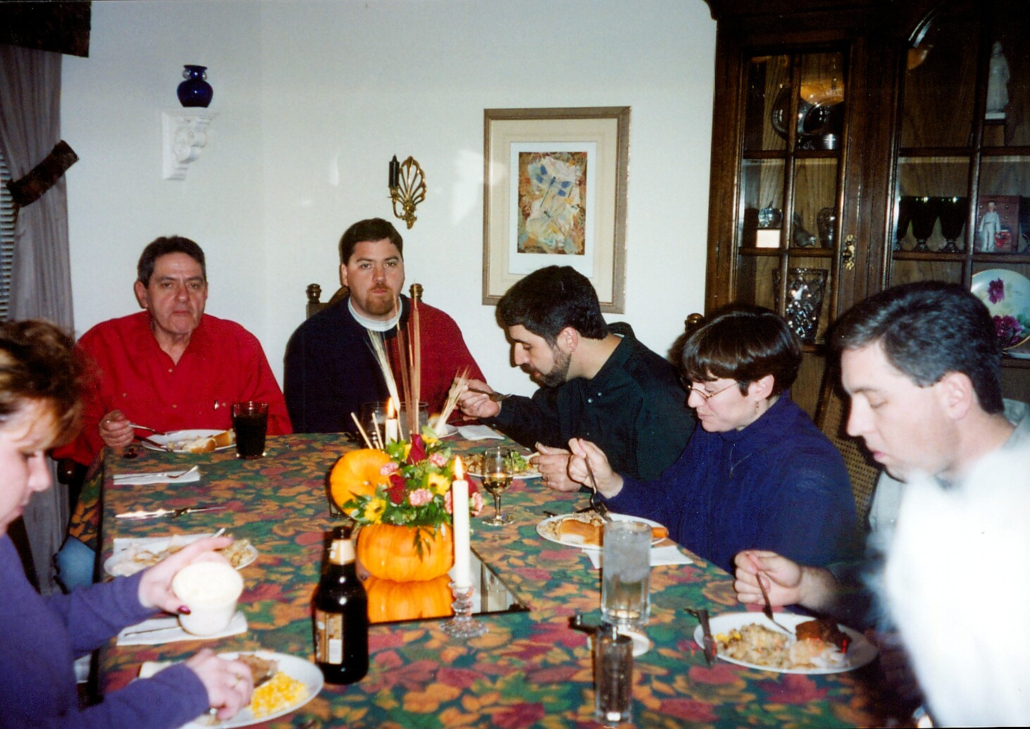 Family gathered for dinner around a table with a pumpkin centerpiece and candles in a home dining room.”