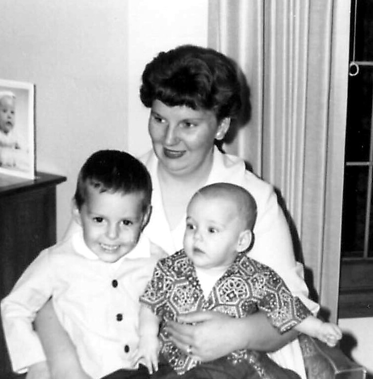 A woman holds a smiling young boy and a baby inside a home for a family photo.