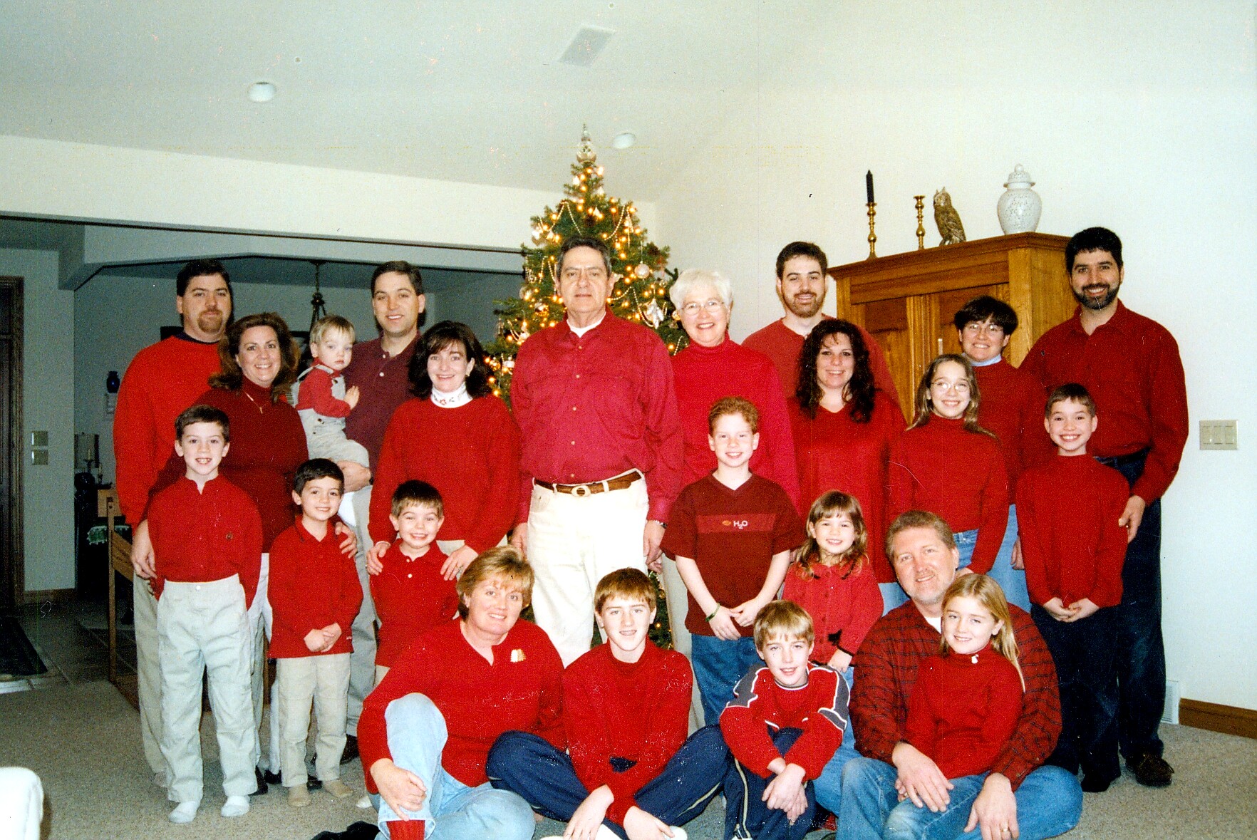 Family group portrait indoors around a decorated Christmas tree; everyone wears red.