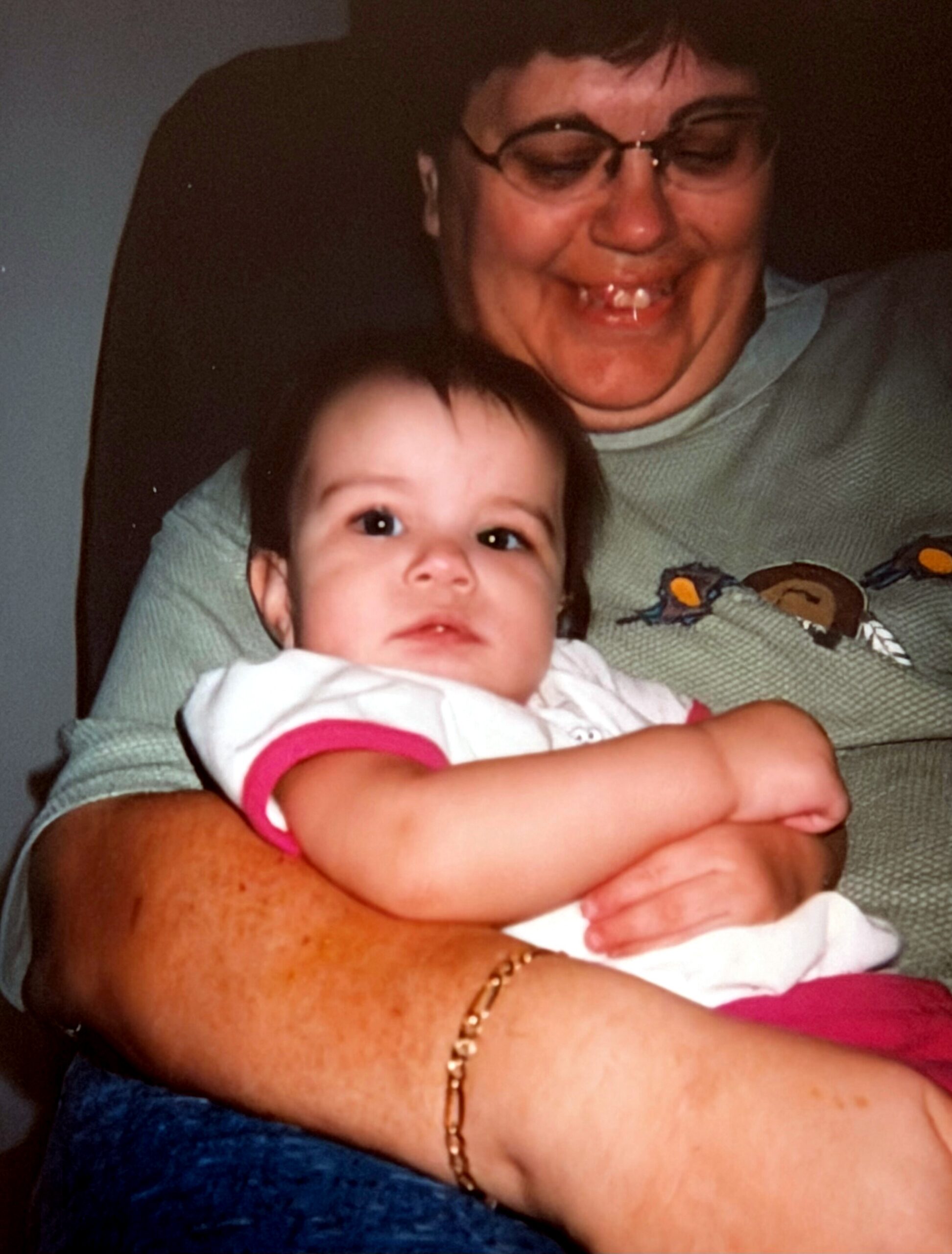 Smiling grandmother wearing glasses gently holding a baby girl in her arms.