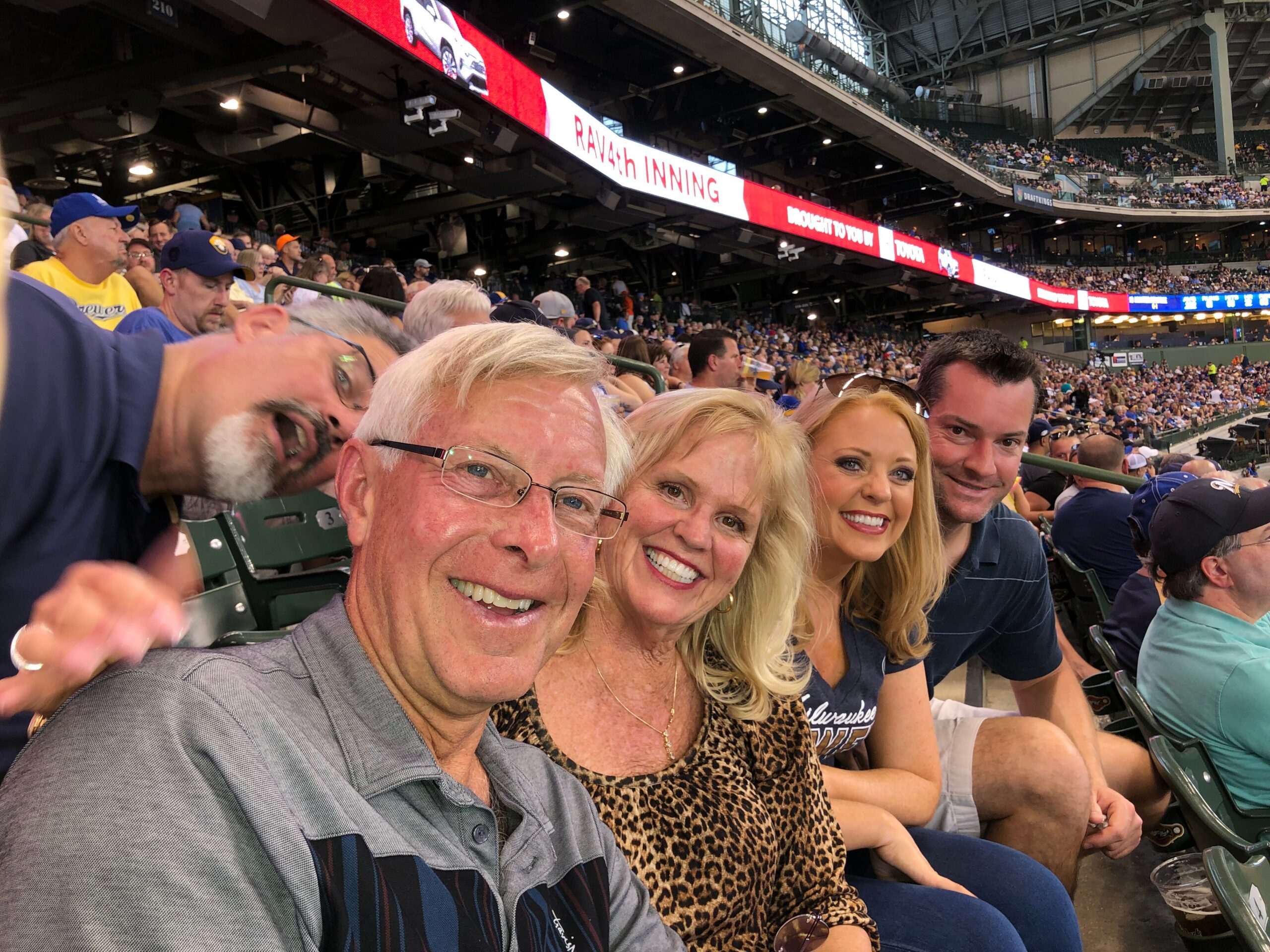 Group of smiling spectators taking a selfie at a crowded baseball stadium.