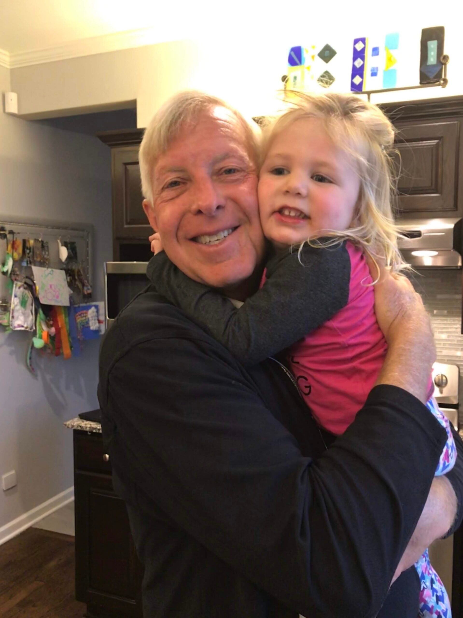 Grandfather and granddaughter sharing a warm hug in a home kitchen, both smiling.
