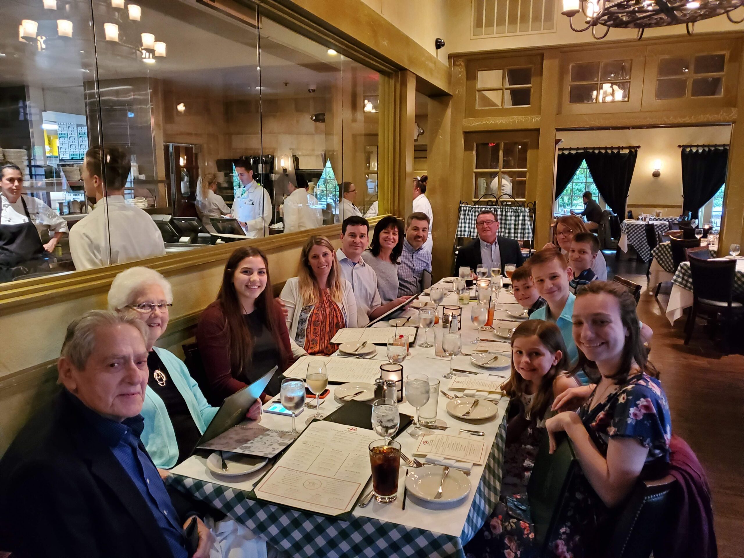 Group of people dining together at a long, checkered table with menus and drinks in a warm restaurant.