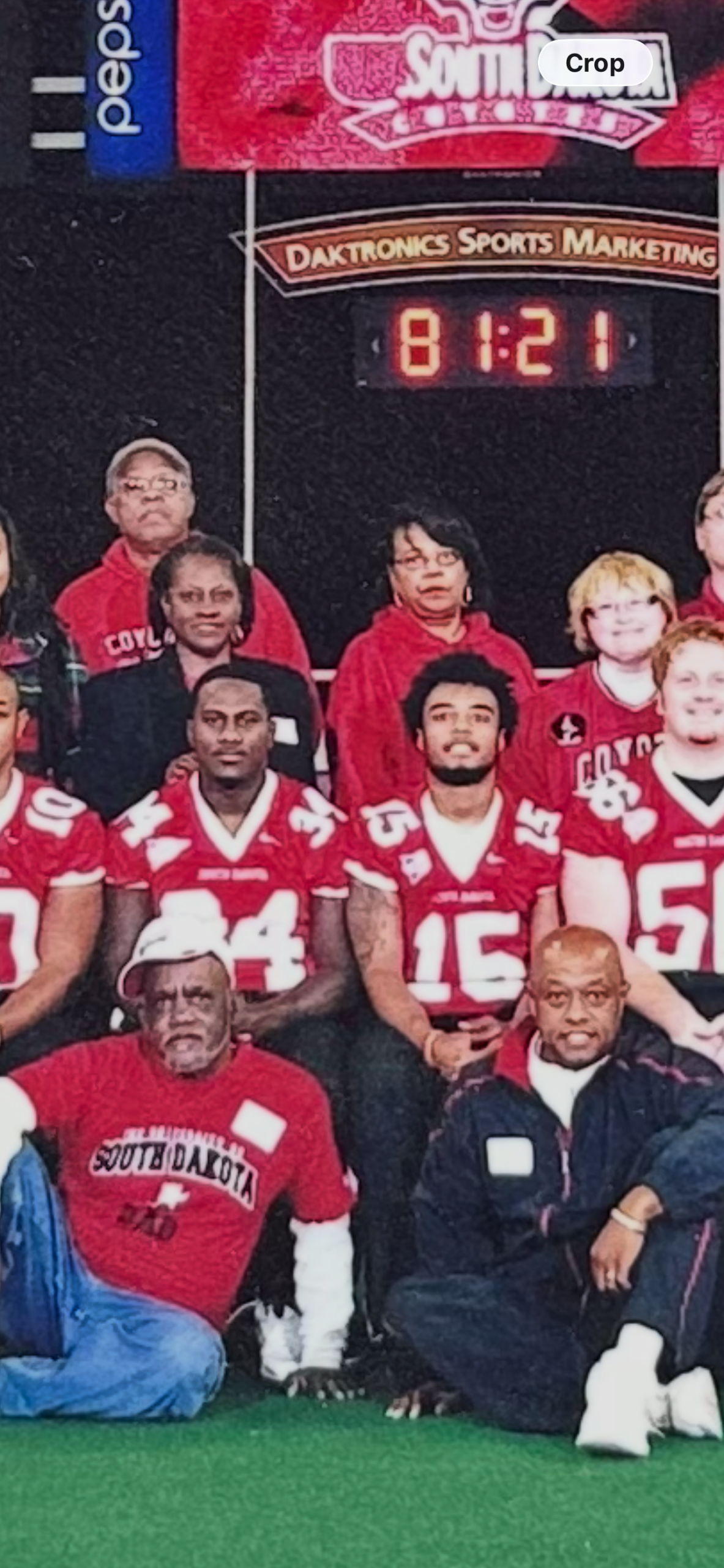Group of football players and coaches posing for a team photo on a field, all in red uniforms with numbers visible.